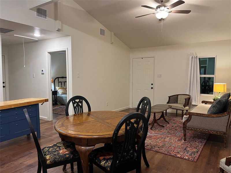 Spacious room featuring vaulted ceilings, wood-finish flooring, a ceiling fan with integrated lighting, and multiple windows with vertical blinds