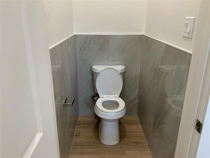 Bathroom featuring a textured wall, wood finished floors, wainscoting, and tile walls Bathroom featuring a textured wall, wood finished floors, wainscoting, and tile walls