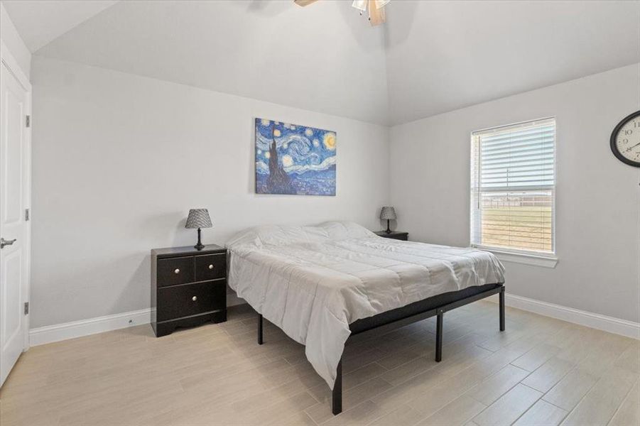 Bedroom featuring lofted ceiling, light wood-type flooring, a ceiling fan, and baseboards