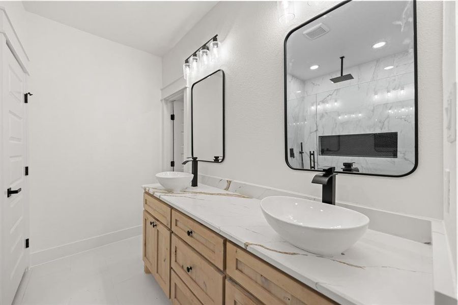 Bathroom with a marble finish shower, double vanity, and light tile patterned flooring