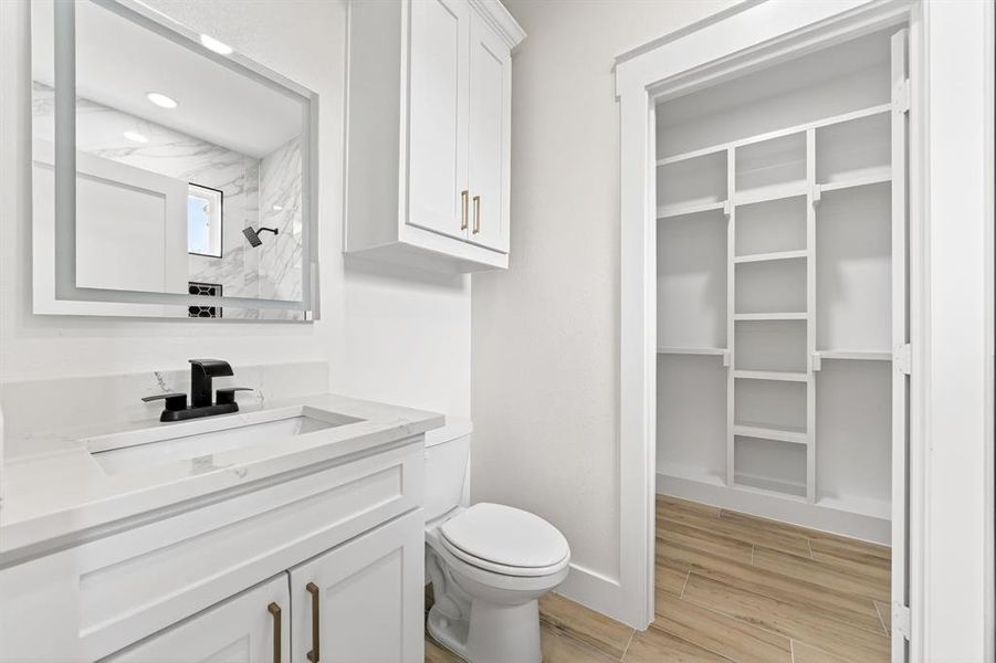 Bathroom featuring a vanity with a white countertop and integrated sink, a modern black faucet, and an illuminated mirror Bathroom featuring a vanity with a white countertop and integrated sink, a modern black faucet, and an illuminated mirror