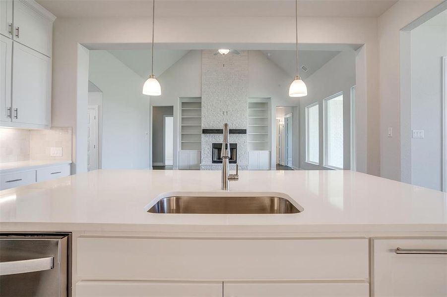 Kitchen featuring pendant lighting, white cabinets, vaulted ceiling, backsplash, and a stone fireplace