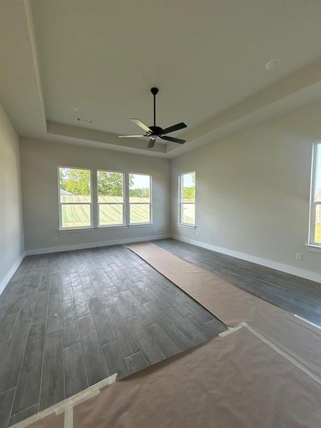 Spacious room featuring a tray ceiling with a ceiling fan, recessed lighting, multiple windows, and wood-look tile flooring Spacious room featuring a tray ceiling with a ceiling fan, recessed lighting, multiple windows, and wood-look tile flooring