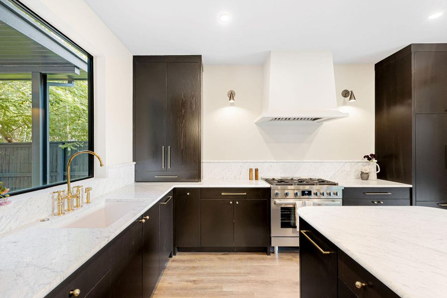 Kitchen with custom range hood, light stone countertops, gas stove, light wood-type flooring, and dark brown cabinets Kitchen with custom range hood, light stone countertops, gas stove, light wood-type flooring, and dark brown cabinets
