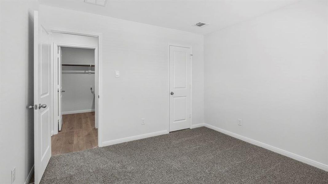 Unfurnished bedroom with a walk in closet and dark colored carpet