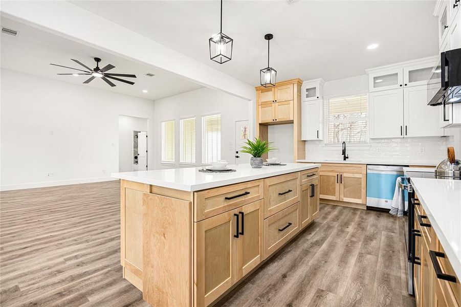 This photo showcases a modern, open-concept kitchen and living area. The kitchen features a large island with light wood cabinetry, white countertops, and pendant lighting. Hardwood floors create a warm ambiance, and the space is bright with ample natural light.