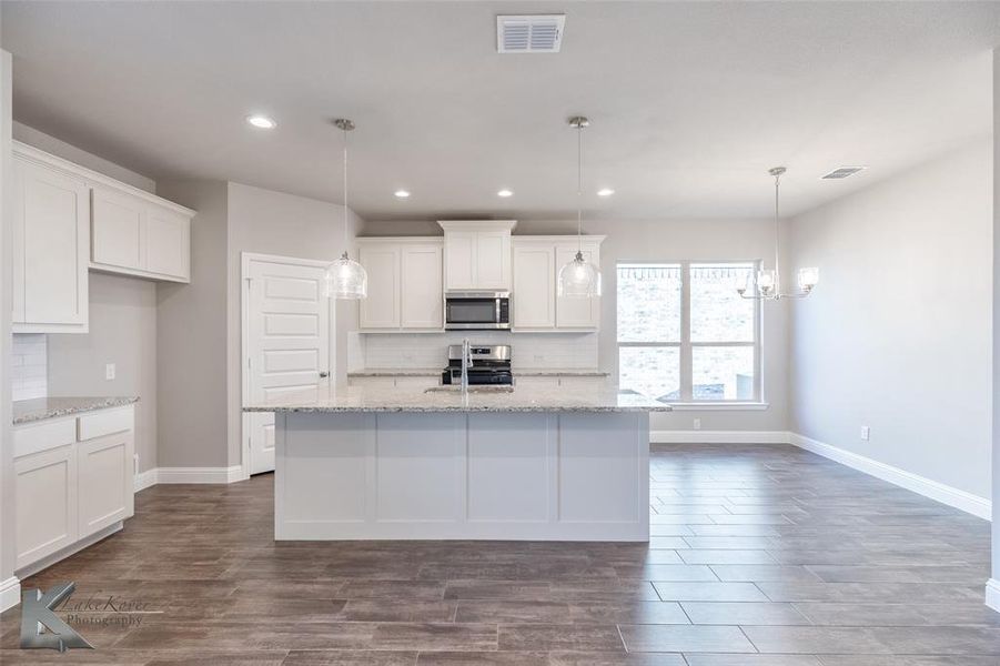 Kitchen with decorative backsplash, light granite counters, white cabinets, decorative light fixtures, and recessed lighting