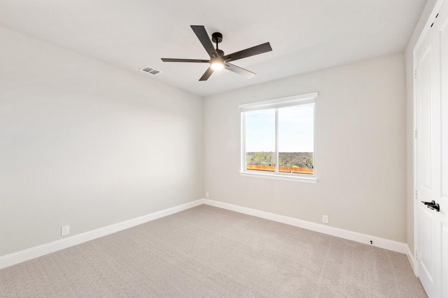 Empty bedroom with gray carpet, white walls, ceiling fan, and single window with outdoor view