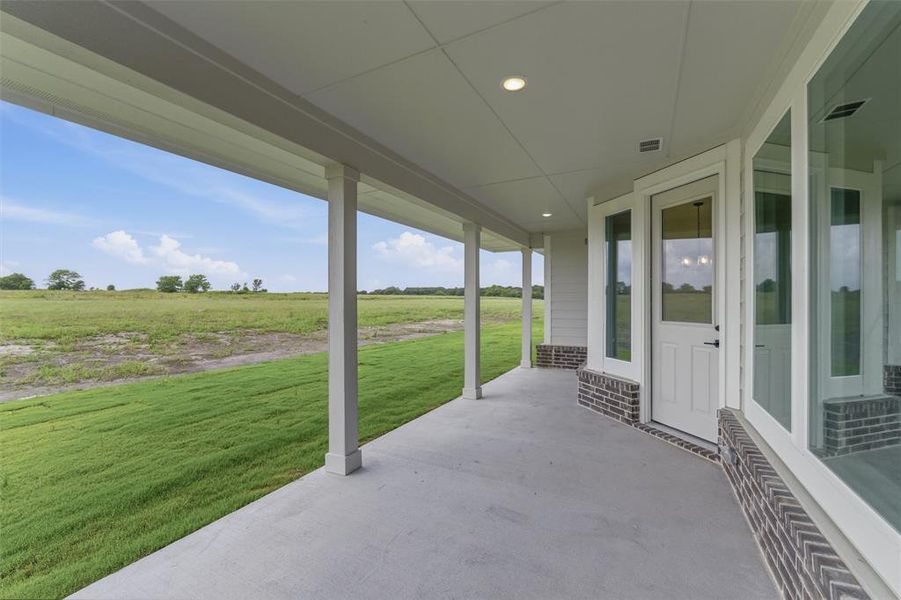 Covered rear patio with concrete flooring, recessed lighting, white columns, and expansive green field surroundings Covered rear patio with concrete flooring, recessed lighting, white columns, and expansive green field surroundings
