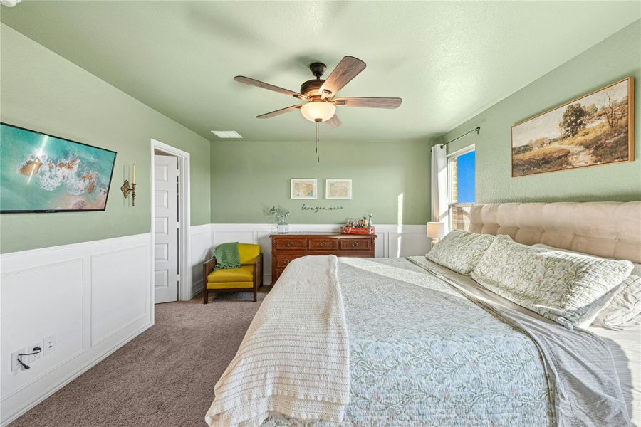 Bedroom with wainscoting, a decorative wall, carpet, and ceiling fan