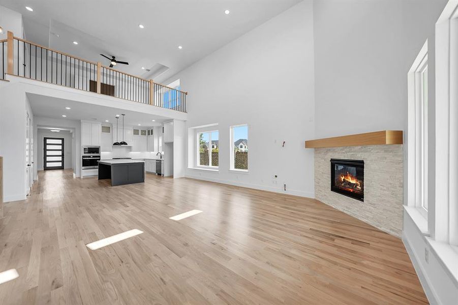 Unfurnished living room with a high ceiling, a fireplace, light wood-style floors, ceiling fan, and recessed lighting