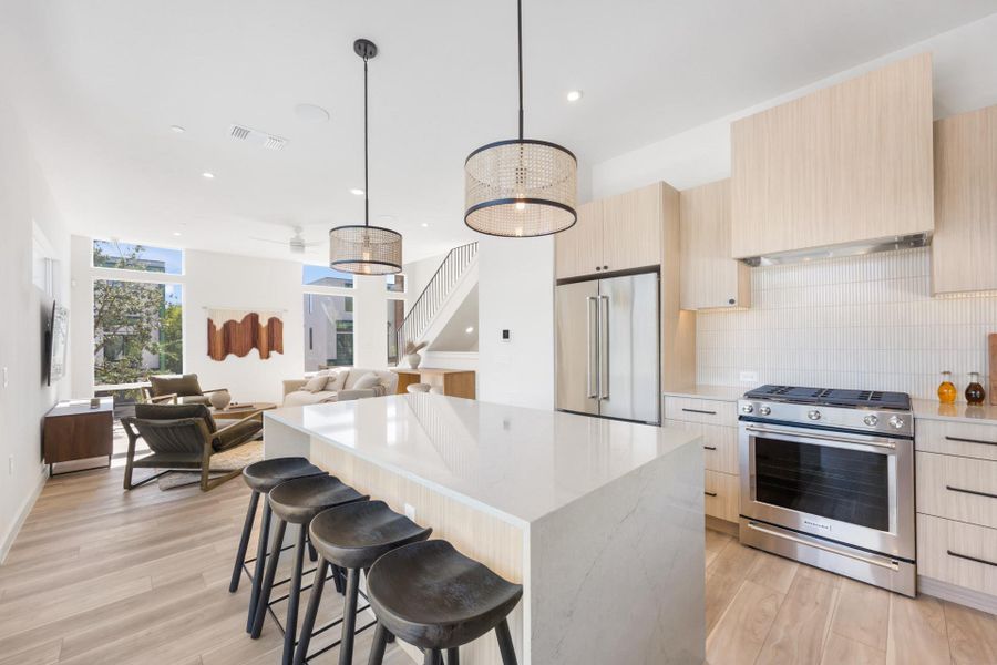 Open-concept living space featuring a central kitchen island with seating, a full suite of stainless steel appliances, light wood-finish cabinetry, and chevron-patterned wood-finish flooring