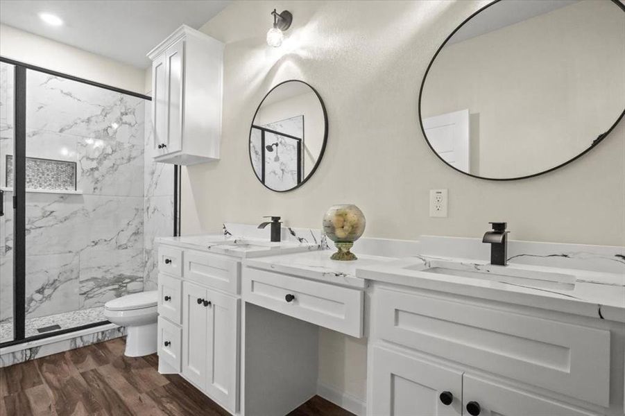 Full bath featuring double vanity, a marble finish shower, and dark wood finished floors Full bath featuring double vanity, a marble finish shower, and dark wood finished floors