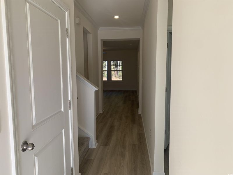 Corridor with light wood finished floors, crown molding, and stairs