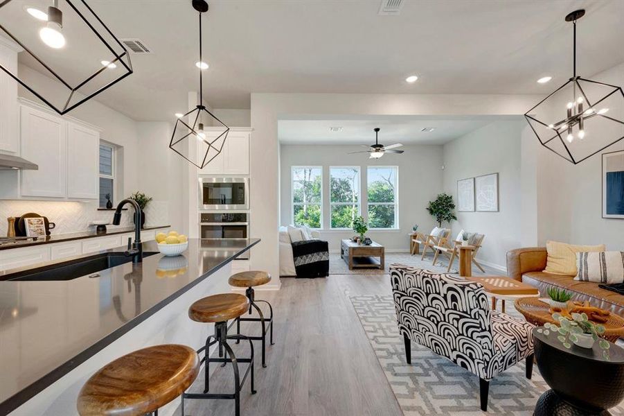 Modern kitchen island with dark countertop and integrated sink, complemented by white cabinetry, stainless steel appliances, and wood-finish flooring extending into the living area