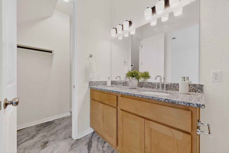 Double vanity with light wood cabinetry, speckled countertop, and chrome fixtures