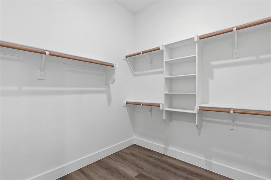 Walk-in closet featuring wood-finish flooring, white baseboards, and built-in white shelving and hanging rods