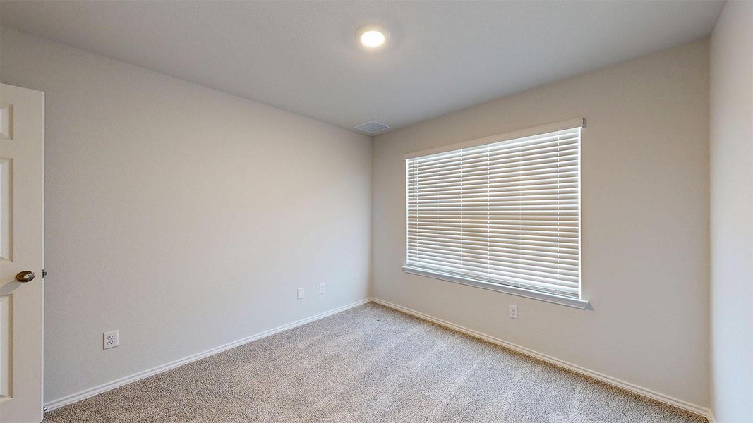 A well-lit bedroom with fresh carpeting and a window offering natural light.