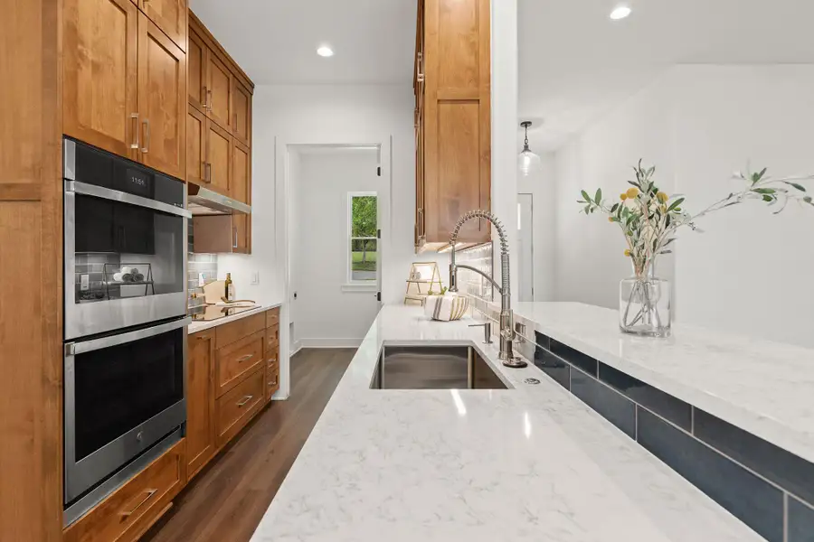 Kitchen with a sink, stainless steel double oven, light stone countertops, dark wood-type flooring, and under cabinet range hood Kitchen with a sink, stainless steel double oven, light stone countertops, dark wood-type flooring, and under cabinet range hood