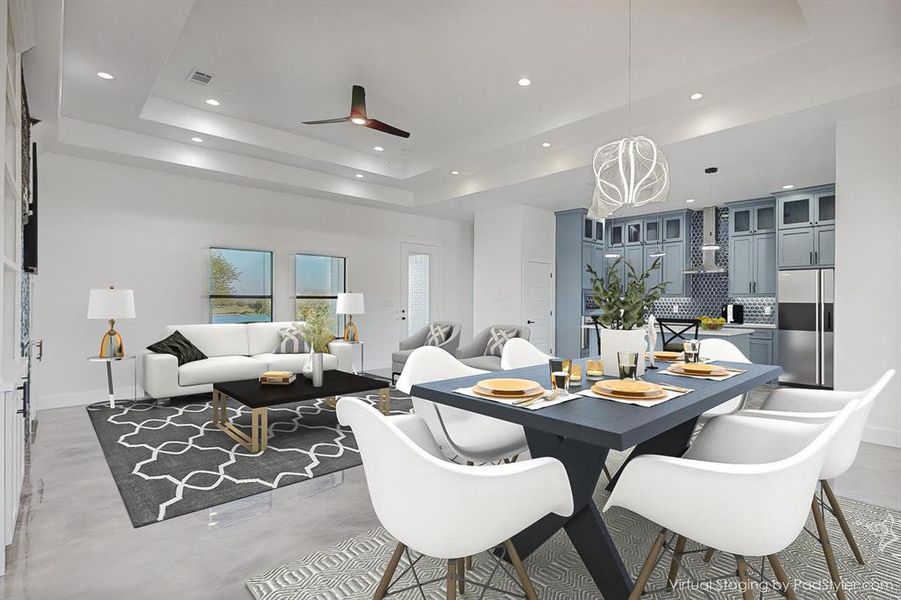 Dining space with concrete floors, ceiling fan with notable chandelier, and a raised ceiling