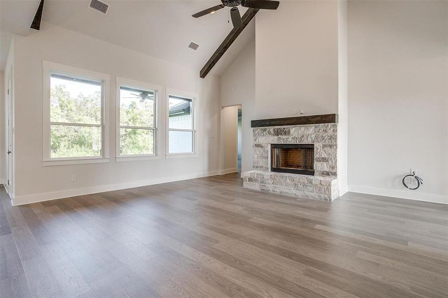 Unfurnished living room featuring ceiling fan, beam ceiling, hardwood / wood-style flooring, and a stone fireplace