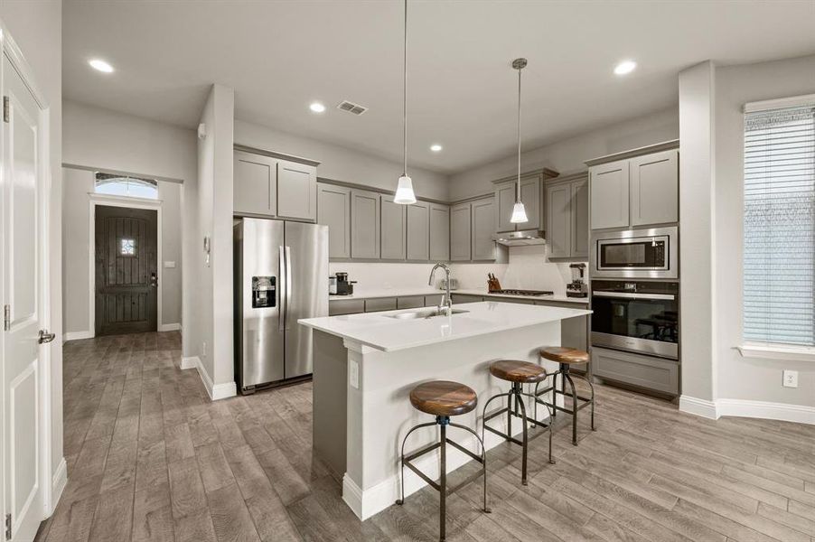 Stunning modern kitchen featuring an oversized island with breakfast bar seating, pendant lighting, sleek quartz countertops, and stainless steel appliances surrounded by ample cabinetry.
