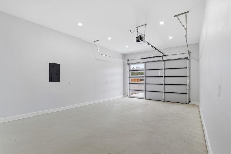 Spacious garage featuring a light gray concrete floor, white walls, recessed ceiling lighting, and a modern glass-paneled garage door with an automatic opener