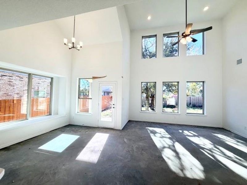Unfurnished living room with plenty of natural light, concrete flooring, ceiling fan, a chandelier, and a high ceiling