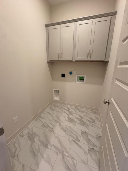 Laundry room featuring light gray cabinetry with brushed nickel hardware, a white tile floor with gray veining, and a paneled interior door Laundry room featuring light gray cabinetry with brushed nickel hardware, a white tile floor with gray veining, and a paneled interior door