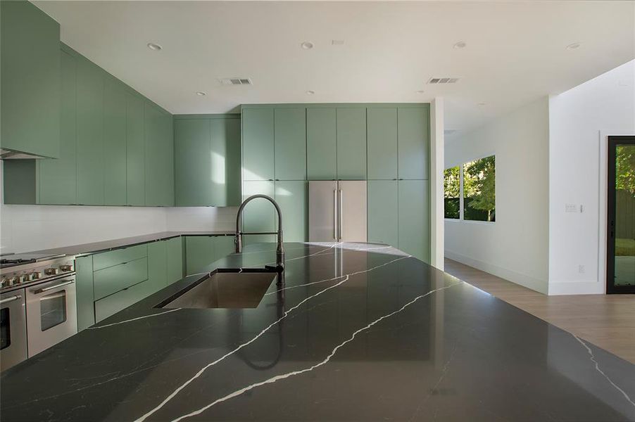 Kitchen with green cabinets, light hardwood / wood-style floors, premium appliances, and sink