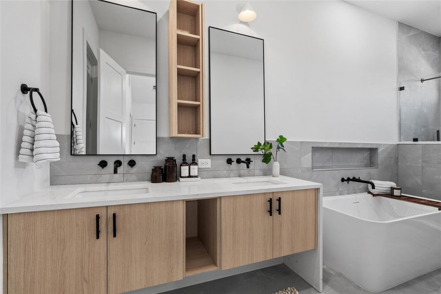 A spa-inspired primary bath defined by floating cabinetry and clean material transitions, where a dual-vanity layout and freestanding soaking tub are arranged for both efficiency and visual balance.