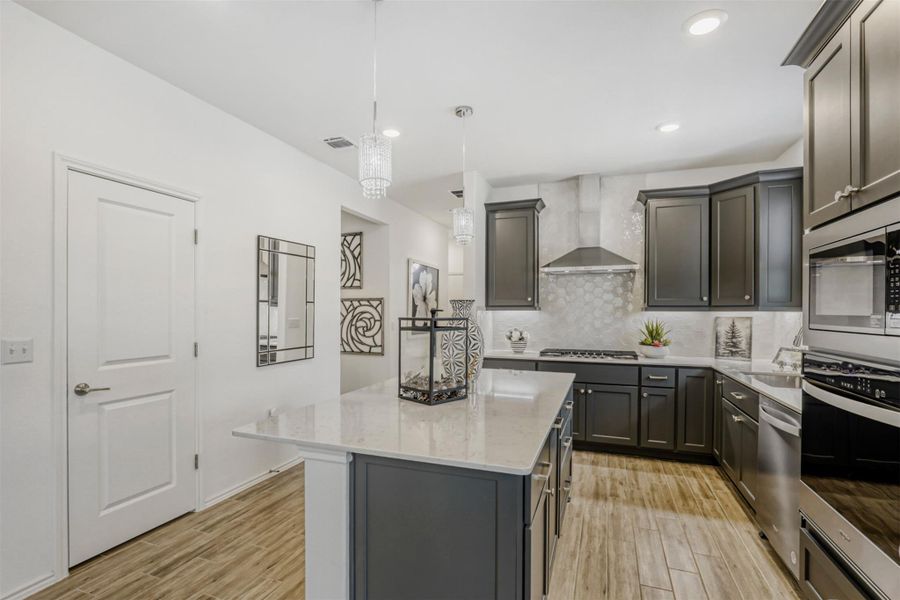 Kitchen featuring pendant lighting, canned lighting, stainless steel appliances, light stone counters, a kitchen island, and light wood-type flooring