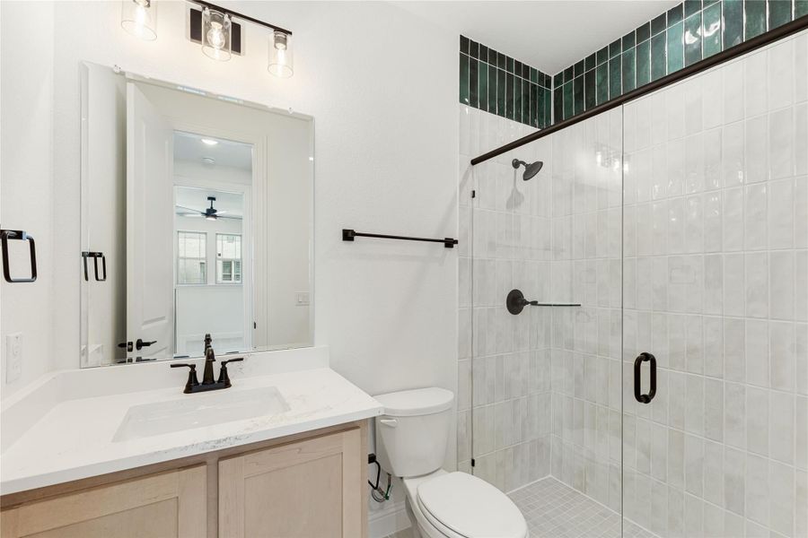 Bathroom with single vanity, walk-in glass shower with white and green tile, and black hardware accents Bathroom with single vanity, walk-in glass shower with white and green tile, and black hardware accents