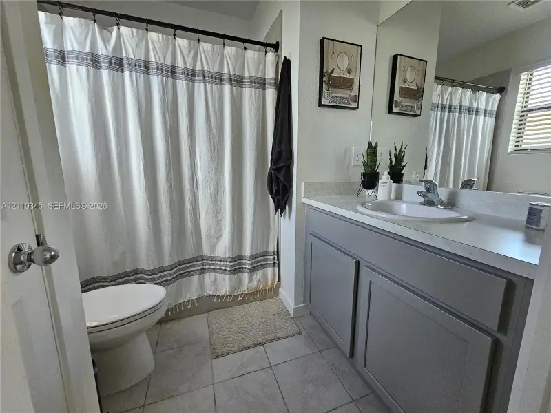 Bathroom featuring a gray shaker-style vanity, stone-finish countertop with an undermount sink, ceramic tile flooring, and a full-width mirror