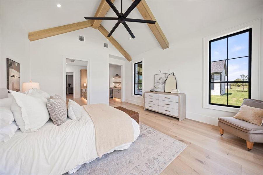 Bedroom with high vaulted ceiling, beamed ceiling, light wood finished floors, and ensuite bathroom