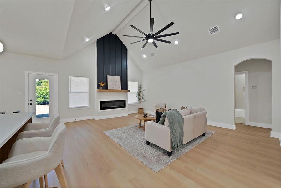Living room with a fireplace, high vaulted ceiling, light wood-style floors, arched walkways, and ceiling fan Living room with a fireplace, high vaulted ceiling, light wood-style floors, arched walkways, and ceiling fan