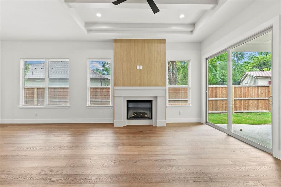 Spacious interior featuring wood-finish flooring, a contemporary fireplace with a light wood-finish surround, and a tray ceiling