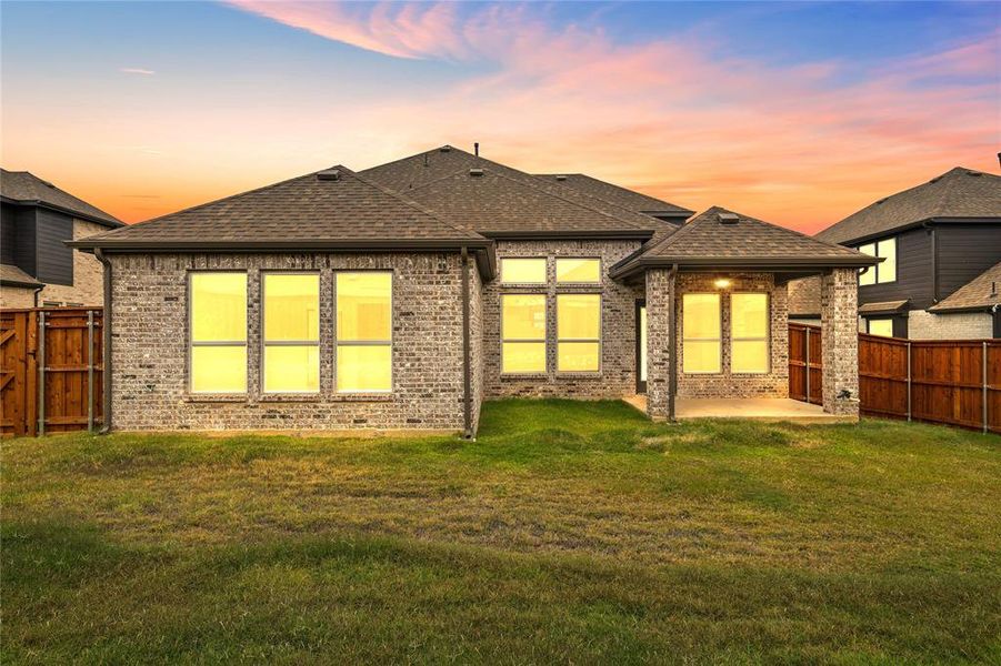 Back house at dusk with a patio and a lawn