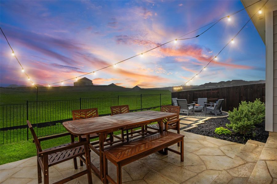 Expansive outdoor patio featuring flagstone paving, a built-in fire pit area with stone pavers, and string lighting overhead