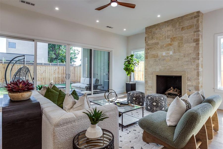 Living room with light hardwood / wood-style floors, ceiling fan, and a stone fireplace