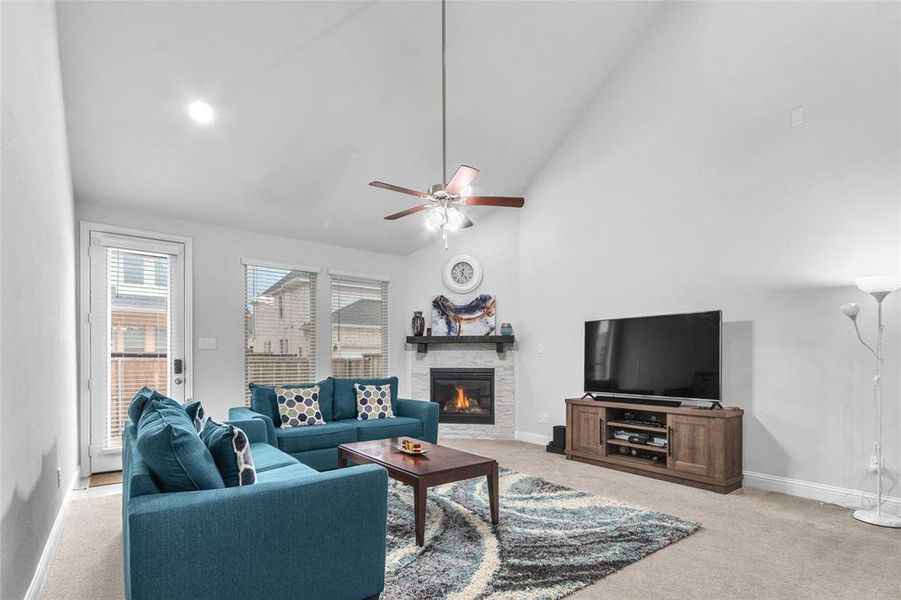 Living area with light carpet, baseboards, high vaulted ceiling, and a stone fireplace