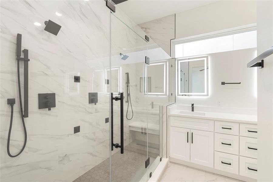 This is a modern bathroom featuring a spacious walk-in shower with glass doors, elegant marble wall tiles, dual shower heads, and a sleek vanity with ample storage and backlit mirrors.