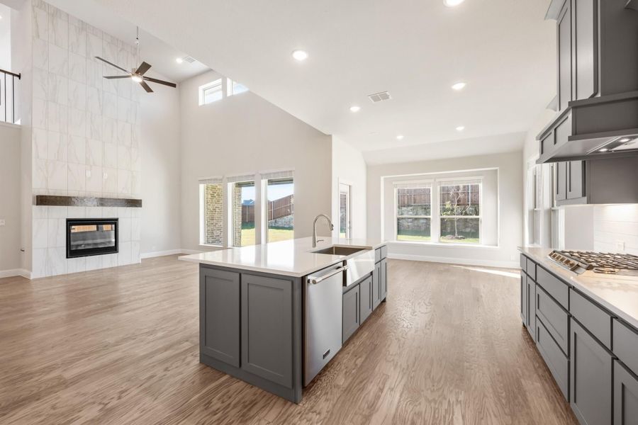 Open kitchen with gray cabinets, center island, and vaulted ceiling open to living area with tiled fireplace Open kitchen with gray cabinets, center island, and vaulted ceiling open to living area with tiled fireplace