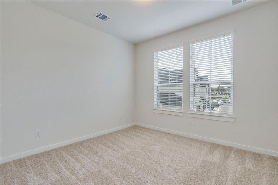 A well-lit bedroom features plush carpeting and multiple windows.