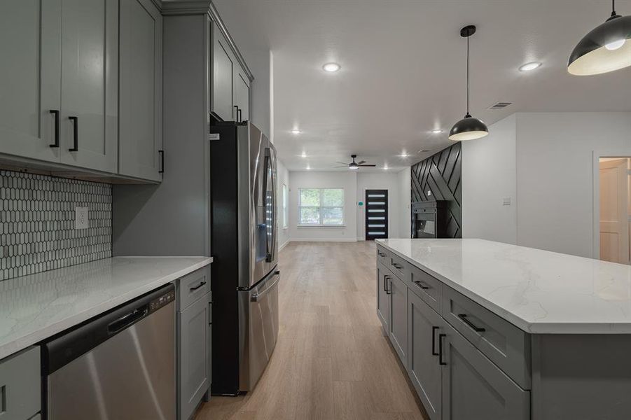 Kitchen with appliances with stainless steel finishes, gray cabinetry, light wood finished floors, light stone countertops, and a ceiling fan Kitchen with appliances with stainless steel finishes, gray cabinetry, light wood finished floors, light stone countertops, and a ceiling fan