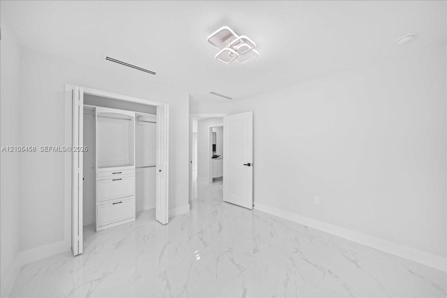 White tile flooring with subtle veining, modern ceiling light fixture, bi-fold closet doors, built-in closet organization with drawers, and a solid interior door White tile flooring with subtle veining, modern ceiling light fixture, bi-fold closet doors, built-in closet organization with drawers, and a solid interior door