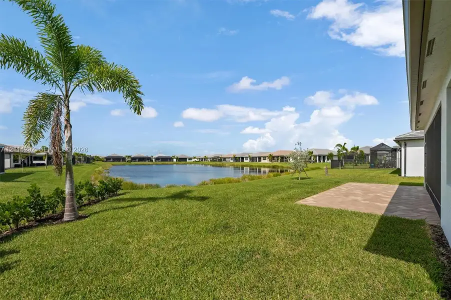 Spacious backyard featuring a paver patio, established palm tree, manicured lawn, and water frontage