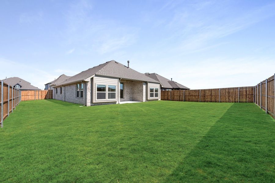 Backyard of brick home with large green lawn and wood privacy fence on both sides Backyard of brick home with large green lawn and wood privacy fence on both sides