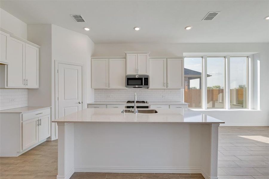 Kitchen featuring a center island with sink, white cabinetry, sink, and tasteful backsplash