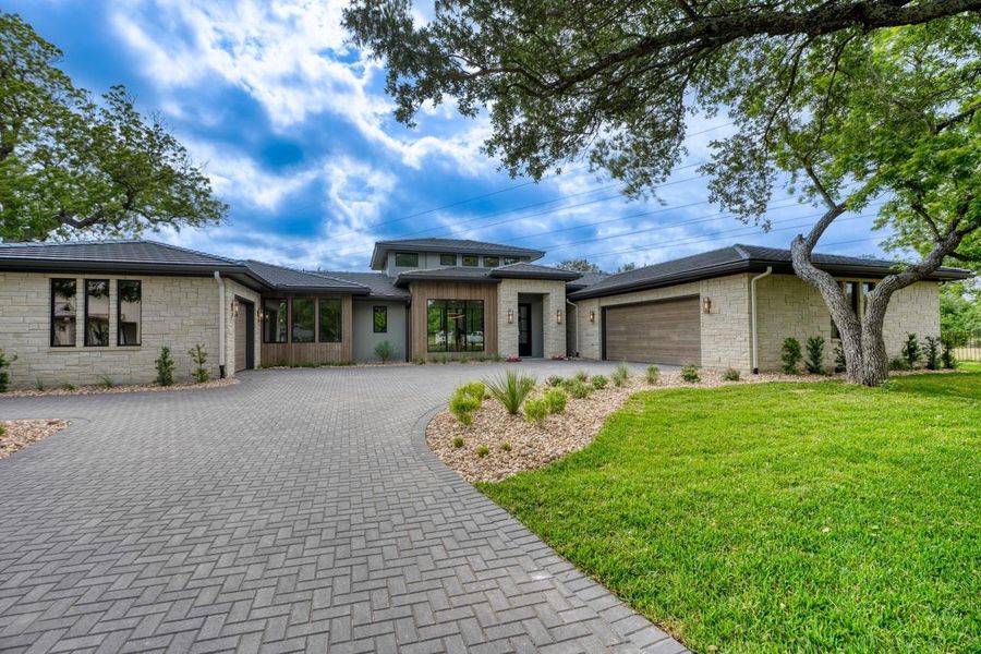 Prairie-style home featuring an attached garage, curved driveway, stone siding, and a front yard